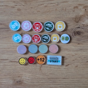May include: A collection of colorful game tokens and markers. The tokens feature various designs, including a chat bubble, cherry blossom, Japanese torii gate, sushi, shopping bag, and a smiley face. The rectangular marker says "START".