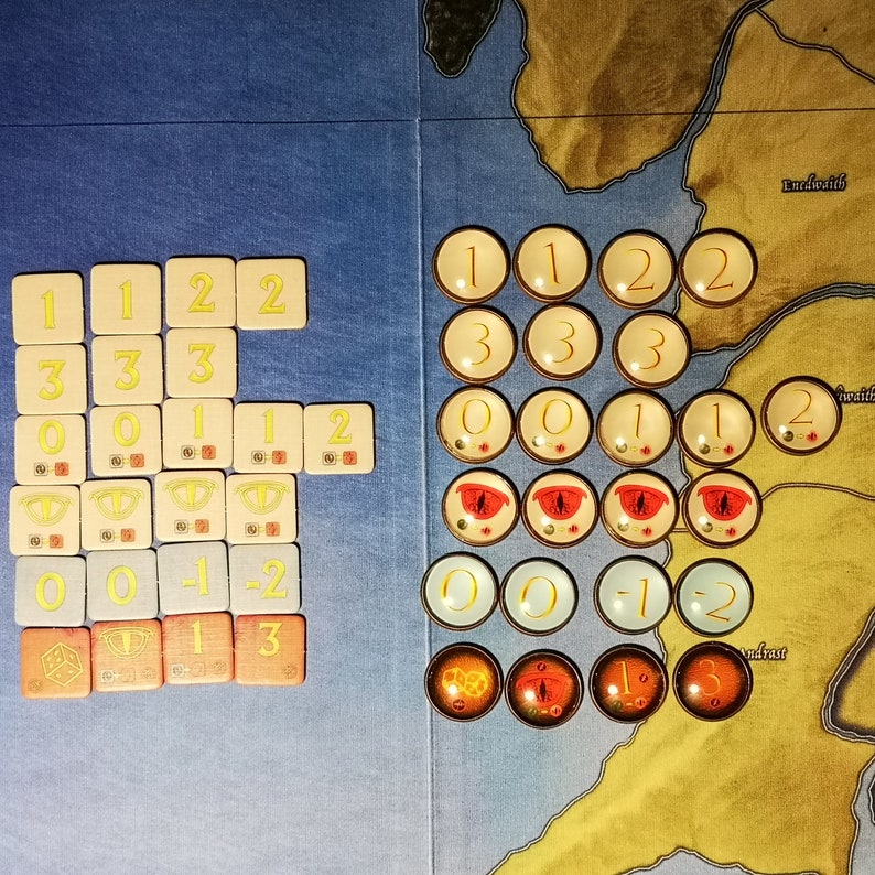 Puede incluir: Un tablero de juego con una variedad de fichas y dados de colores. Las fichas est&aacute;n numeradas del 0 al 3 y tienen un ojo rojo en el centro. Los dados est&aacute;n numerados del 1 al 3 y son amarillos con n&uacute;meros negros. El tablero est&aacute; dividido en secciones con diferentes nombres, incluyendo "Enedwaith" y "Andrast".