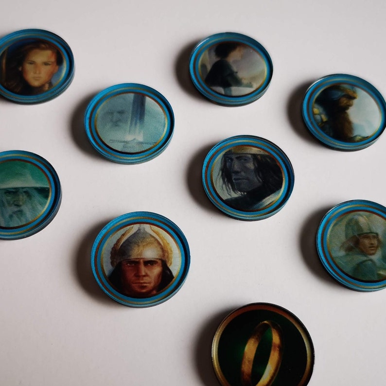 Puede incluir: Nueve fichas redondas azules y doradas con im&aacute;genes de personajes y objetos de El Se&ntilde;or de los Anillos. Las fichas presentan im&aacute;genes de Gandalf, Aragorn, Frodo, el Anillo &Uacute;nico, y m&aacute;s.