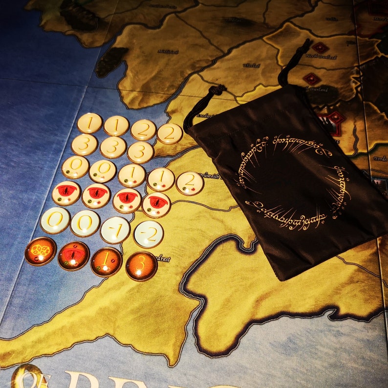 May include: A brown cloth bag with the inscription "One Ring to rule them all, One Ring to find them, One Ring to bring them all and in the darkness bind them" and a set of 20 round tokens with numbers and red and yellow symbols.