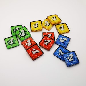 May include: A collection of 12 colorful game tiles with a starburst design. Each tile features a number, either "1" or "2", with a plus sign before the number. The tiles are in various colors, including red, blue, green, and yellow.