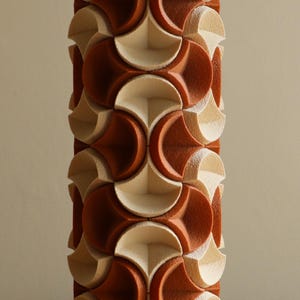 May include: A tall, geometric lamp with a repeating pattern of terracotta and cream-colored shapes. The lamp's design features a series of interlocking, curved elements, creating a textured surface. The lamp is a decorative lighting fixture.