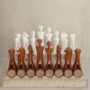 Könnte beinhalten: Ein modernes Schachspiel mit braunen und weißen Figuren. Die braunen Figuren haben ein einzigartiges, abstraktes Design, während die weißen Figuren traditioneller sind. Das Set wird auf einem Brett in Betonoptik präsentiert, was eine minimalistische Ästhetik schafft.