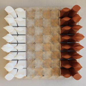Op de afbeelding: Abstract vierkant kunstwerk met een rasterpatroon. De linkerkant heeft witte, bladachtige vormen, terwijl de rechterkant bruine, gedraaide vormen heeft. Het midden heeft een getextureerd, vierkant patroon in bruin- en beigetinten.