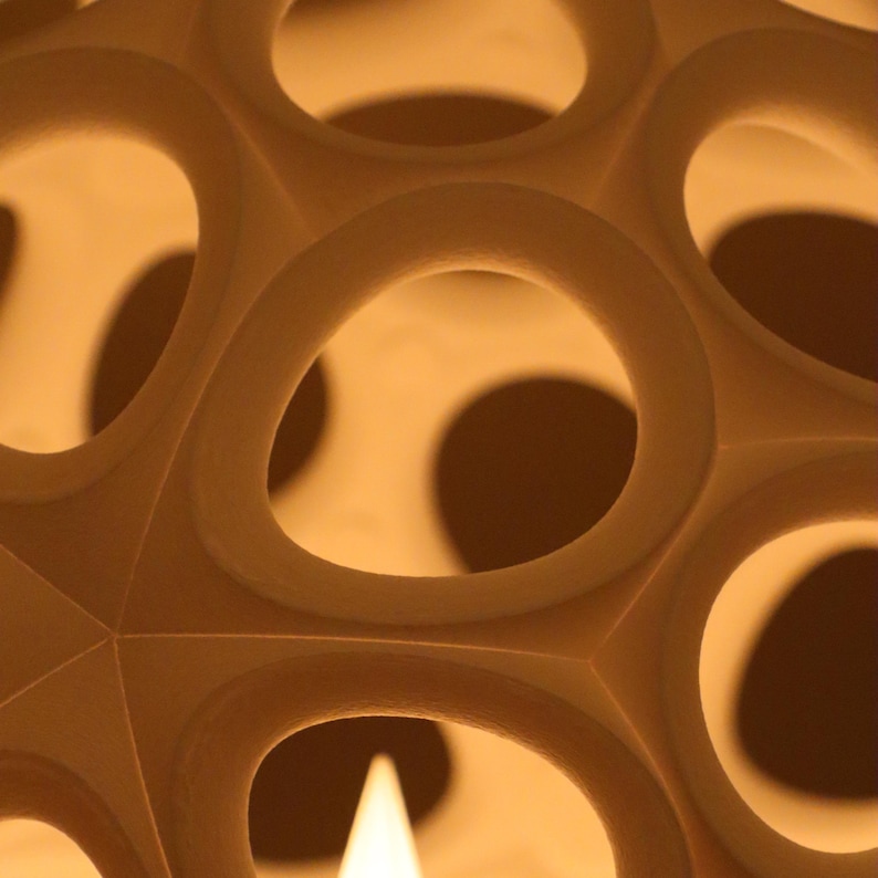 May include: Close-up of a beige, spherical object with a geometric design. The object has a series of circular openings, creating a pattern of light and shadow. The overall effect is a modern, abstract design.