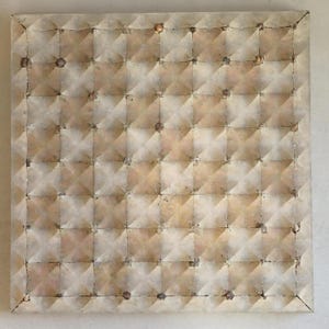 Op de afbeelding: Vierkant kunstwerk met een herhalend patroon van verhoogde, ruitvormige secties. Het oppervlak heeft een getextureerde, verouderde uitstraling met beige, bruin en bruin tinten. Kleine, donkere vlekken zijn verspreid over het oppervlak.