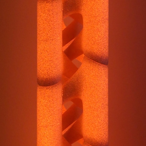May include: A vertical cylindrical object with a textured orange surface featuring a repeating spiral cutout pattern. The structure has a glowing appearance with darker shaded edges along the interior curves of the spiral design.