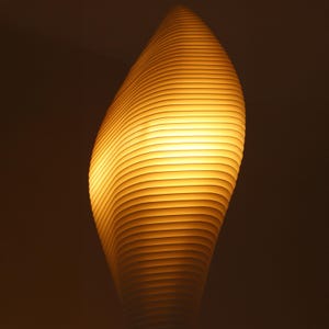 May include: A modern, abstract lamp with a warm, yellow glow. The lamp's design features a series of horizontal, curved lines that create a layered effect. The lamp's shape is reminiscent of a flame or a stylized leaf.