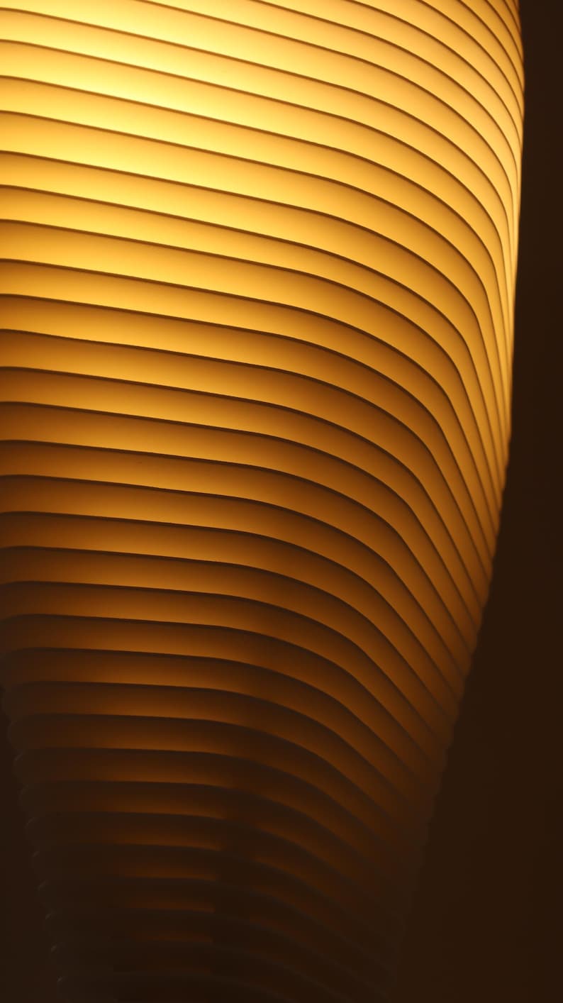 May include: Abstract image of a cylindrical object with horizontal, curved lines. The object has a warm, golden-yellow glow, with darker shadows creating depth. The design suggests a modern, architectural theme.