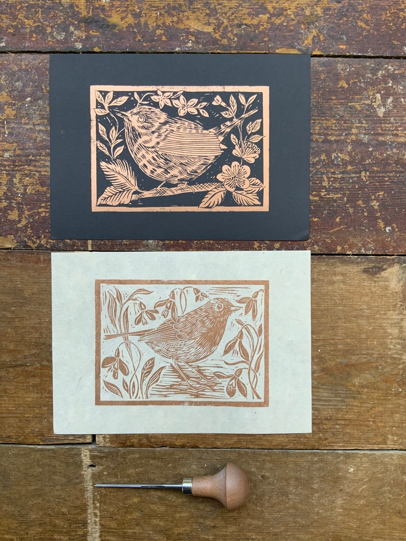 Puede incluir: Dos grabados en madera de un p&aacute;jaro en un entorno floral. La impresi&oacute;n superior est&aacute; en papel negro y la inferior en papel blanco. Ambas impresiones son de color cobre.