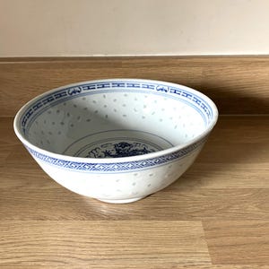 May include: White porcelain bowl with blue floral and geometric patterns. The bowl has a pierced design and a blue rim. The bowl is sitting on a wooden surface.