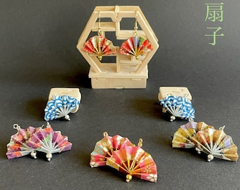 May include: A set of six pairs of fan earrings. The earrings are made of paper and feature a variety of colorful patterns. The earrings are displayed on a wooden stand. The text "Fan Earrings" and "扇子" are visible in the image.