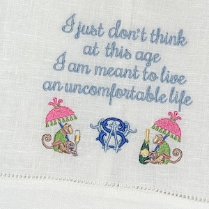 May include: Embroidered kitchen towel with a quote that reads "I just don't think at this age I am meant to live an uncomfortable life". The towel features two monkeys holding champagne glasses and an umbrella, and a monogram.