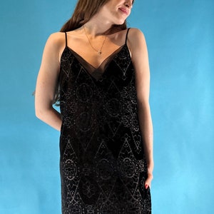 Puede incluir: Un vestido negro de satén con un patrón geométrico. El vestido tiene un escote en V y tirantes finos.