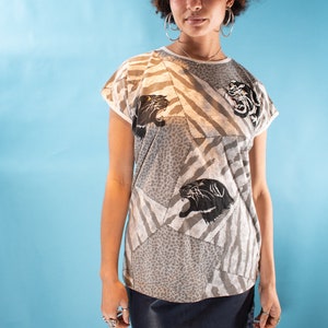 May include: A woman wearing a grey and white patterned short-sleeved shirt with black panther print and a dark blue leather skirt.