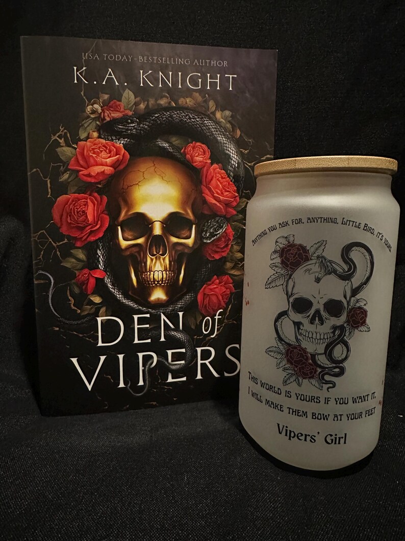 May include: A book titled "Den of Vipers" by K.A. Knight, featuring a skull and snake design, and a frosted glass tumbler with a skull, rose, and snake design. The tumbler has text that reads "Vipers' Girl".