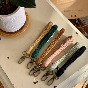 May include: Six colorful crocheted keychains with gold metal key rings. The keychains are in shades of green, brown, pink, and beige.