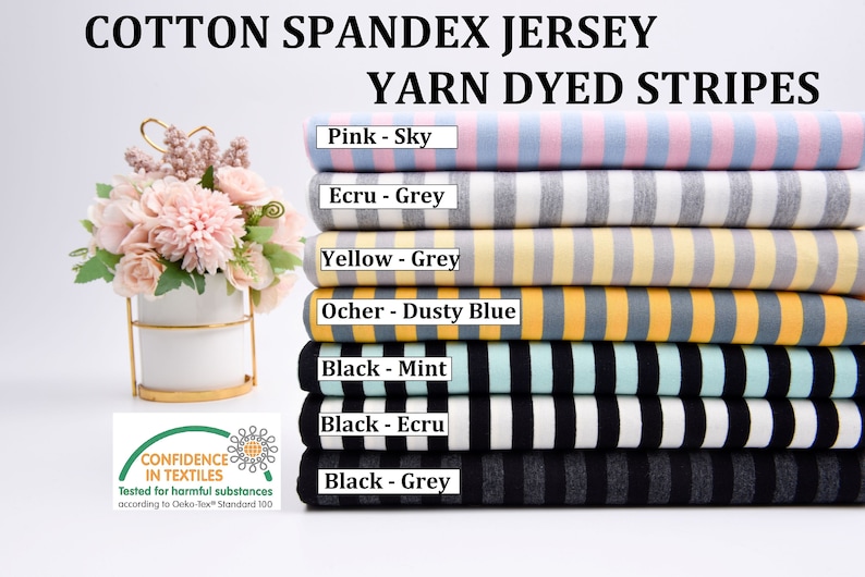 May include: A stack of six cotton spandex jersey fabrics with yarn dyed stripes in various color combinations. The colors include pink, sky blue, ecru, grey, yellow, dusty blue, black, mint, and black. The fabric is tested for harmful substances according to Oeko-Tex Standard 100.