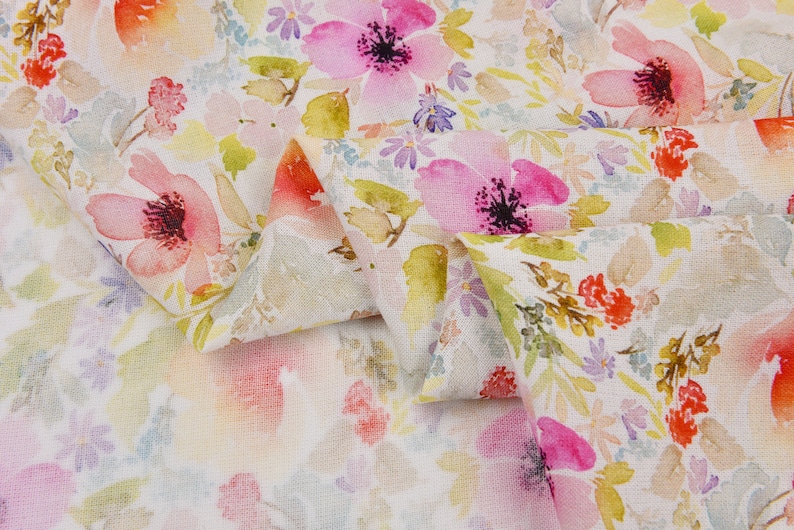 Peut inclure: Tissu blanc avec un imprim&eacute; floral aquarelle repr&eacute;sentant des fleurs roses, rouges et jaunes. Le tissu est pli&eacute; en deux, montrant le motif des deux c&ocirc;t&eacute;s.