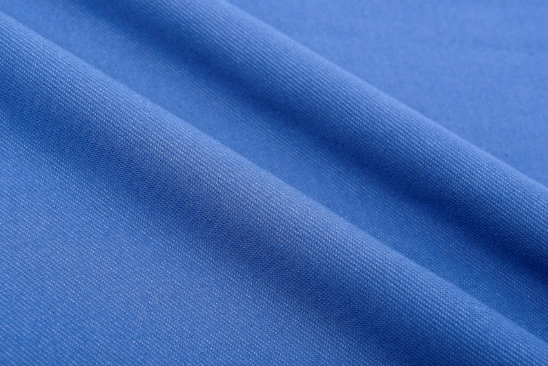 May include: Close-up of a textured, bright blue fabric with diagonal folds. The fabric has a subtle woven pattern, creating a sense of depth and texture. The color is a vibrant, solid blue, suitable for apparel or home decor.