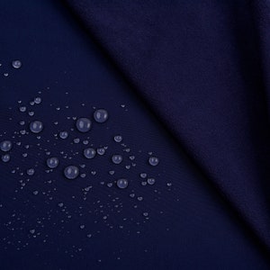 K&ouml;nnte beinhalten: Nahaufnahme eines marineblauen Stoffes mit Wassertropfen, die &uuml;ber die Oberfl&auml;che verstreut sind. Der Stoff ist gefaltet und zeigt ein strukturiertes Aussehen. Die Tr&ouml;pfchen sind klar und reflektieren das Licht, wodurch ein Kontrast zum dunklen Hintergrund entsteht.