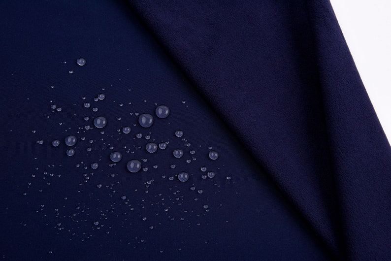 K&ouml;nnte beinhalten: Nahaufnahme eines marineblauen Stoffes mit Wassertropfen, die &uuml;ber die Oberfl&auml;che verstreut sind. Der Stoff ist gefaltet und zeigt ein strukturiertes Aussehen. Die Tr&ouml;pfchen sind klar und reflektieren das Licht, wodurch ein Kontrast zum dunklen Hintergrund entsteht.