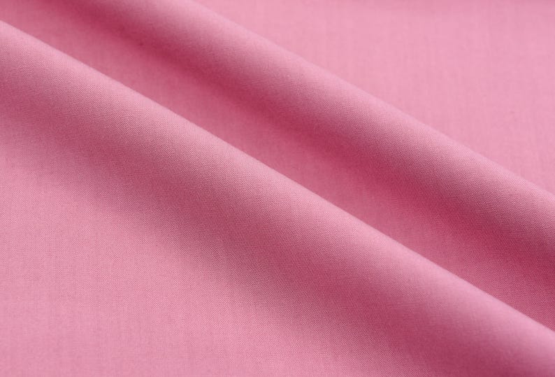 May include: A smooth, soft, pink fabric with a subtle sheen. The fabric is folded in a gentle curve, creating a soft, flowing texture.