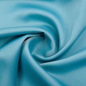 Puede incluir: Primer plano de una muestra de tela turquesa con una superficie texturizada sutil. La tela est&aacute; drapeada y doblada, creando sombras y reflejos suaves. El color es un turquesa vibrante y s&oacute;lido, adecuado para ropa o decoraci&oacute;n del hogar.
