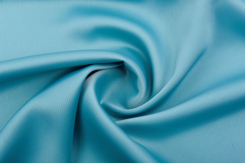 Puede incluir: Primer plano de una muestra de tela turquesa con una superficie texturizada sutil. La tela est&aacute; drapeada y doblada, creando sombras y reflejos suaves. El color es un turquesa vibrante y s&oacute;lido, adecuado para ropa o decoraci&oacute;n del hogar.