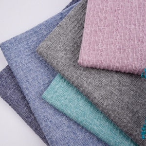 May include: A stack of five fabric swatches in different colors and textures. The top swatch is a light pink with a textured pattern. The other swatches are in shades of blue and green.