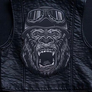 May include: A black leather vest with a silver embroidered patch of a gorilla wearing goggles. The gorilla has an open mouth and sharp teeth.