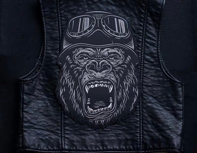 May include: A black leather vest with a silver embroidered patch of a gorilla wearing goggles. The gorilla has an open mouth and sharp teeth.