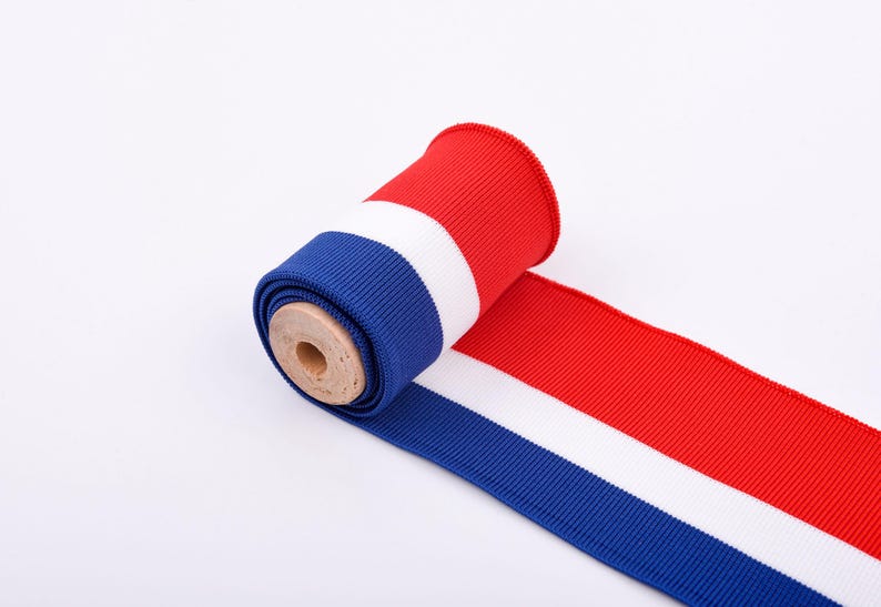 May include: A roll of red, white, and blue ribbon. The ribbon is unrolled, revealing the colors in stripes. The roll is made of a ribbed fabric and is on a white background. The ribbon is likely used for crafts or decorations.