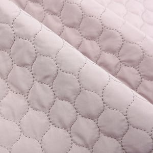 Puede incluir: Primer plano de una tela acolchada de color rosa p&aacute;lido con un patr&oacute;n repetitivo de peque&ntilde;as formas redondeadas. La tela tiene una apariencia suave y texturizada.