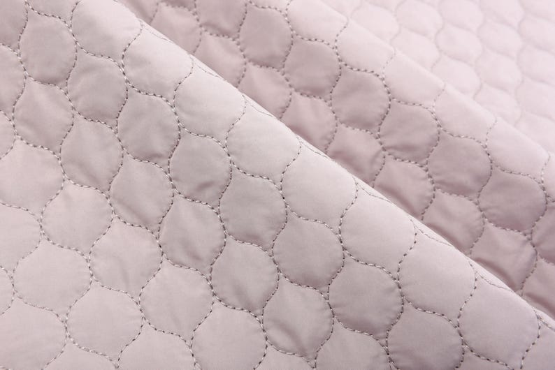 Puede incluir: Primer plano de una tela acolchada de color rosa p&aacute;lido con un patr&oacute;n repetitivo de peque&ntilde;as formas redondeadas. La tela tiene una apariencia suave y texturizada.