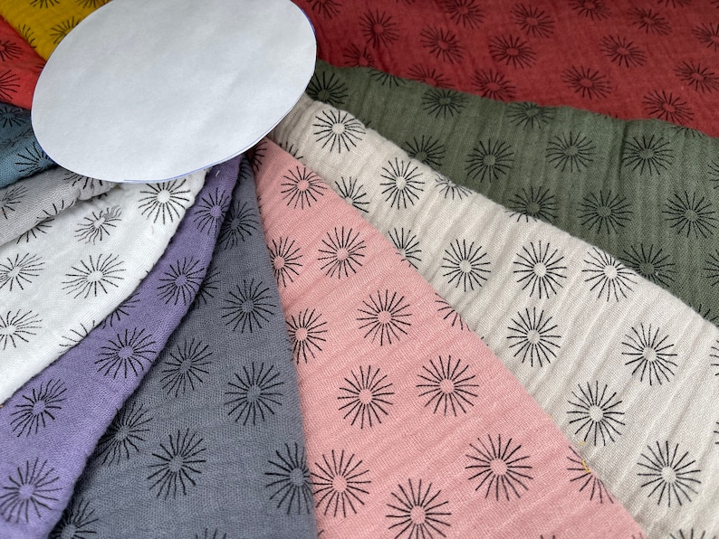 May include: A collection of fabric swatches with a black sunburst pattern on a variety of colors, including red, green, white, pink, gray, and purple.