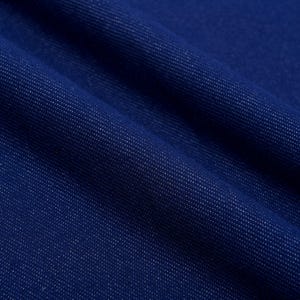 May include: Close-up of a deep blue denim fabric with a diagonal weave pattern. The fabric has a slightly textured surface and is folded, creating shadows and highlights. The color is a rich, saturated blue.