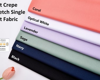 Op de afbeelding: Een close-up van een stapel zachte crepe stretch single knit stof in verschillende kleuren, waaronder koraal, wit, lavendel, salie, marineblauw en zwart. De stof is gecertificeerd met de Oeko-Tex Standard 100.
