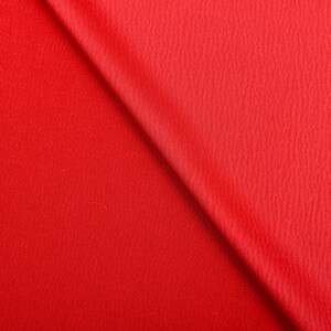 Puede incluir: Primer plano de una tela roja vibrante con una superficie texturizada. La tela est&aacute; doblada diagonalmente, creando un juego de luces y sombras. El material parece ser un textil de peso medio.