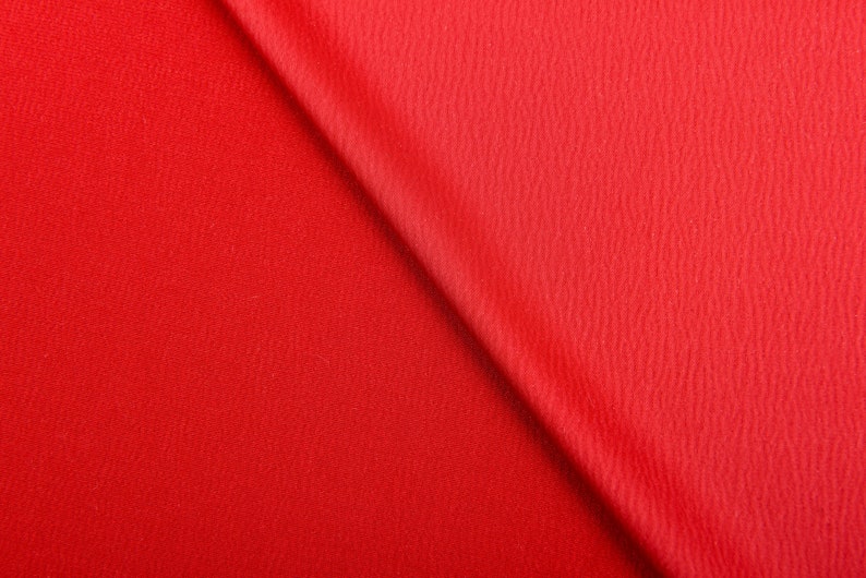 Puede incluir: Primer plano de una tela roja vibrante con una superficie texturizada. La tela est&aacute; doblada diagonalmente, creando un juego de luces y sombras. El material parece ser un textil de peso medio.