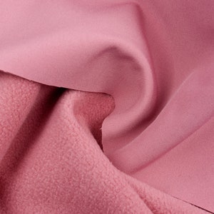 K&ouml;nnte beinhalten: Nahaufnahme von zwei Schichten rosa Stoff. Die obere Schicht ist glatt und flie&szlig;end, w&auml;hrend die untere Schicht ein strukturiertes, fleeceartiges Aussehen hat. Die Farbe ist ein weiches, ged&auml;mpftes Rosa und erzeugt eine warme und einladende &Auml;sthetik.