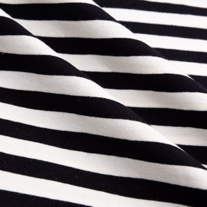 May include: Close-up of black and white striped fabric with a smooth texture. The fabric is folded and has a slight sheen.