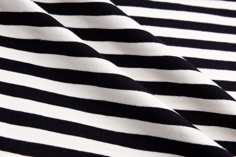 May include: Close-up of black and white striped fabric with a smooth texture. The fabric is folded and has a slight sheen.