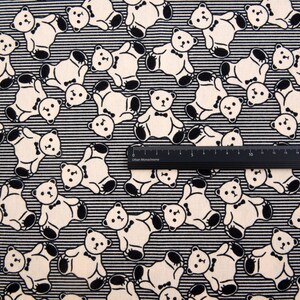 May include: Black and white fabric with a repeating pattern of teddy bears wearing bow ties. The fabric has thin black stripes.