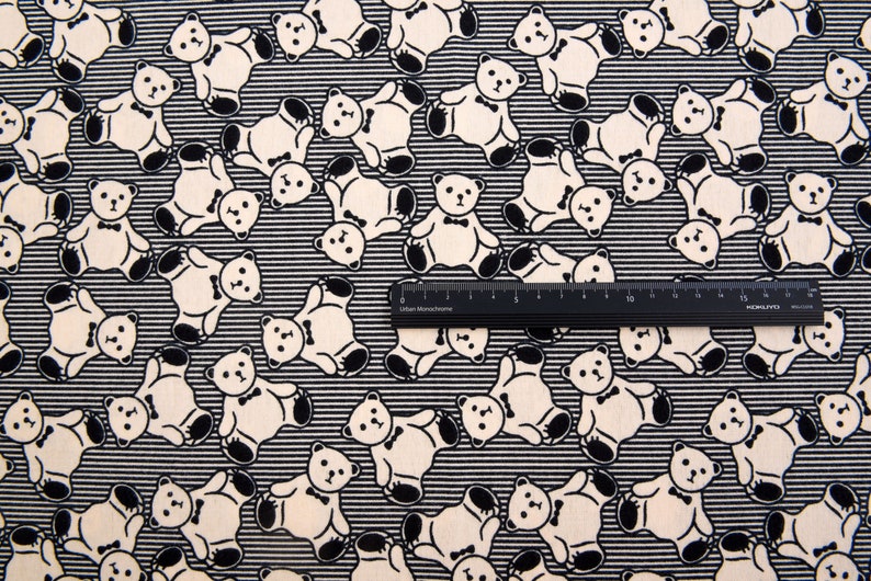 May include: Black and white fabric with a repeating pattern of teddy bears wearing bow ties. The fabric has thin black stripes.
