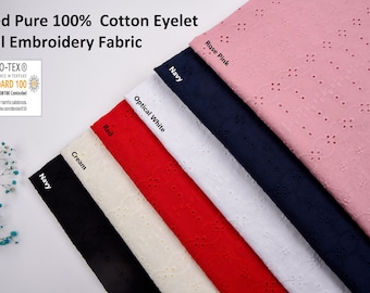 May include: A close-up of a variety of cotton eyelet fabric swatches in different colors, including rose pink, navy, optical white, red, cream, and navy. The fabric has a delicate eyelet pattern and is labeled as "Dyed Pure 100% Cotton Eyelet Voil Embroidery Fabric". The Oeko-Tex Standard 100 logo is also visible.