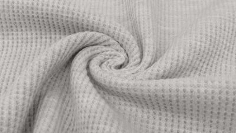 May include: Close-up of a light gray waffle-knit fabric. The fabric is tightly woven with a textured, grid-like pattern. The material is arranged in a swirling, spiral shape, showcasing its drape and texture. The fabric appears soft and pliable.
