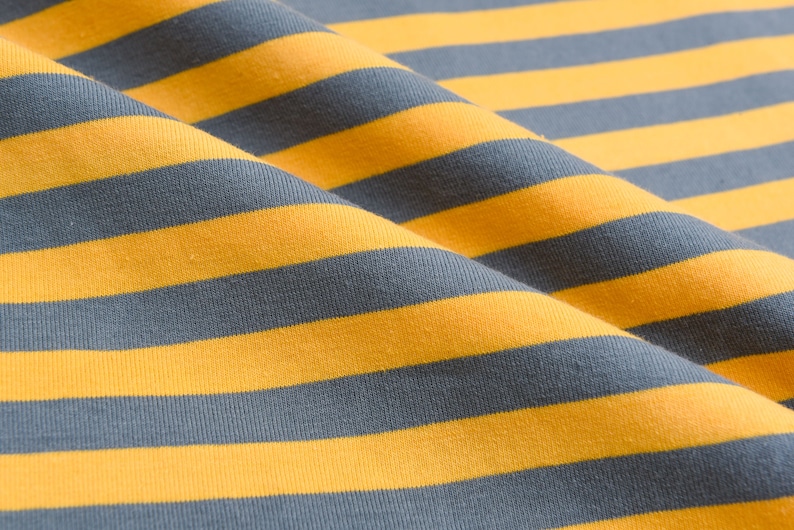 May include: Close-up of a yellow and gray striped fabric. The fabric is folded and has a soft, textured appearance.