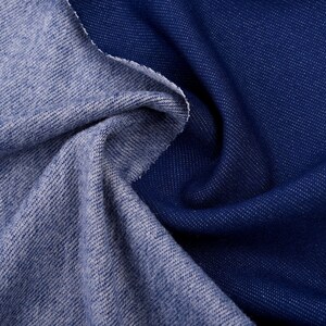 May include: Close-up of two denim fabric swatches. One is a lighter blue, the other is a darker indigo. The fabrics are draped and folded, showing the texture and weave of the material. The edges are raw and unfinished.