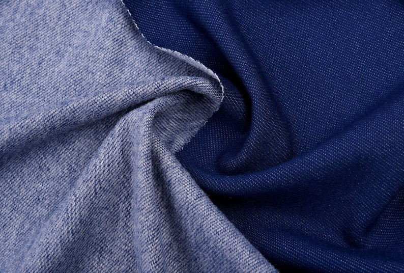 May include: Close-up of two denim fabric swatches. One is a lighter blue, the other is a darker indigo. The fabrics are draped and folded, showing the texture and weave of the material. The edges are raw and unfinished.